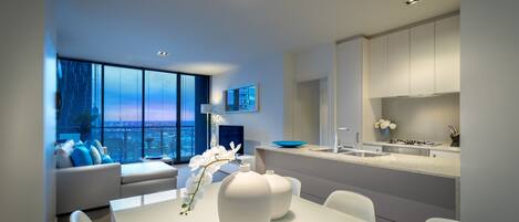 A modern living room with a white sofa, a dining table with chairs, and a view of the city through large windows.