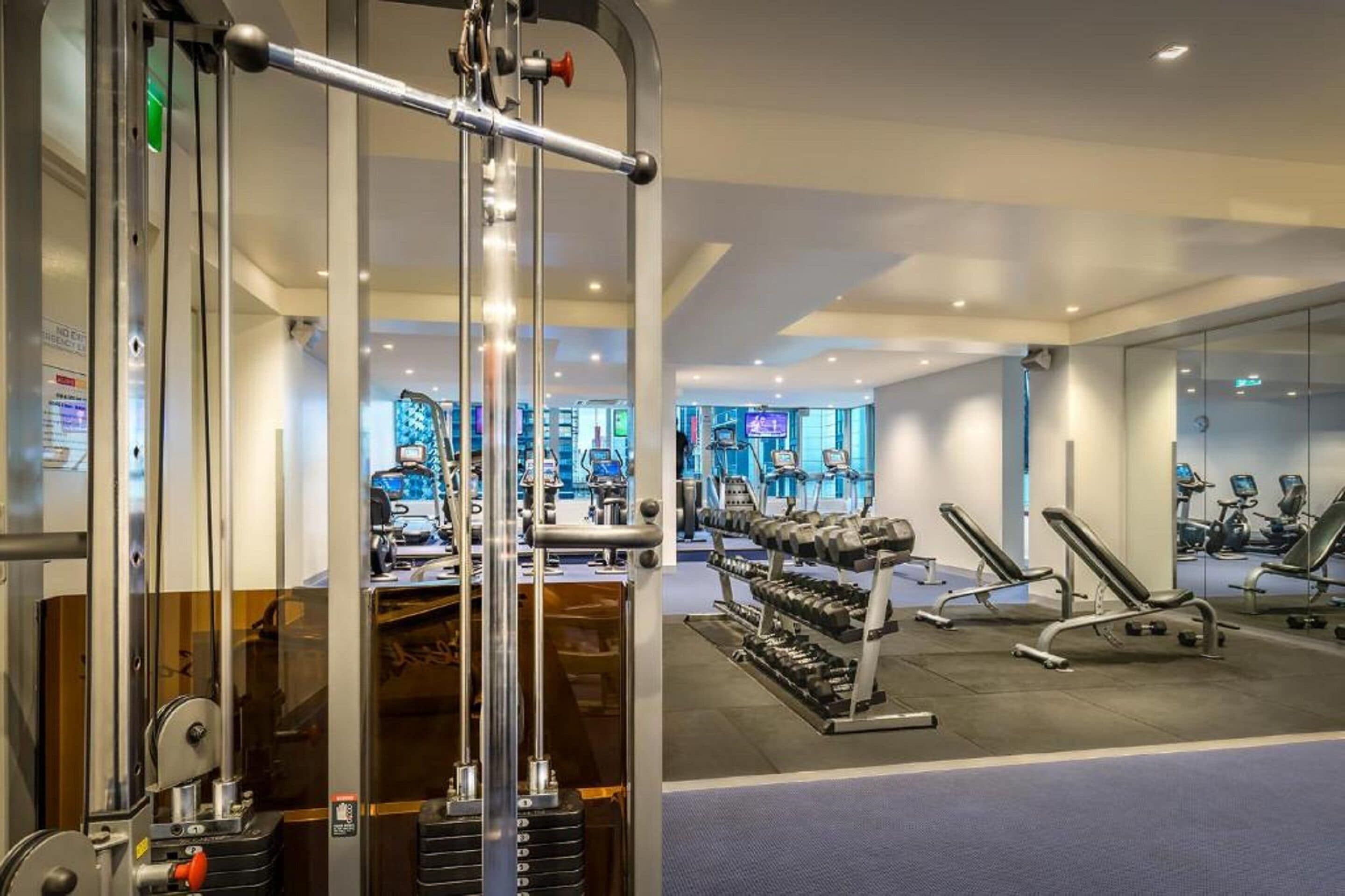 Un gimnasio con equipo de ejercicio, incluyendo una máquina de poleas, mancuernas y bancos de pesas.