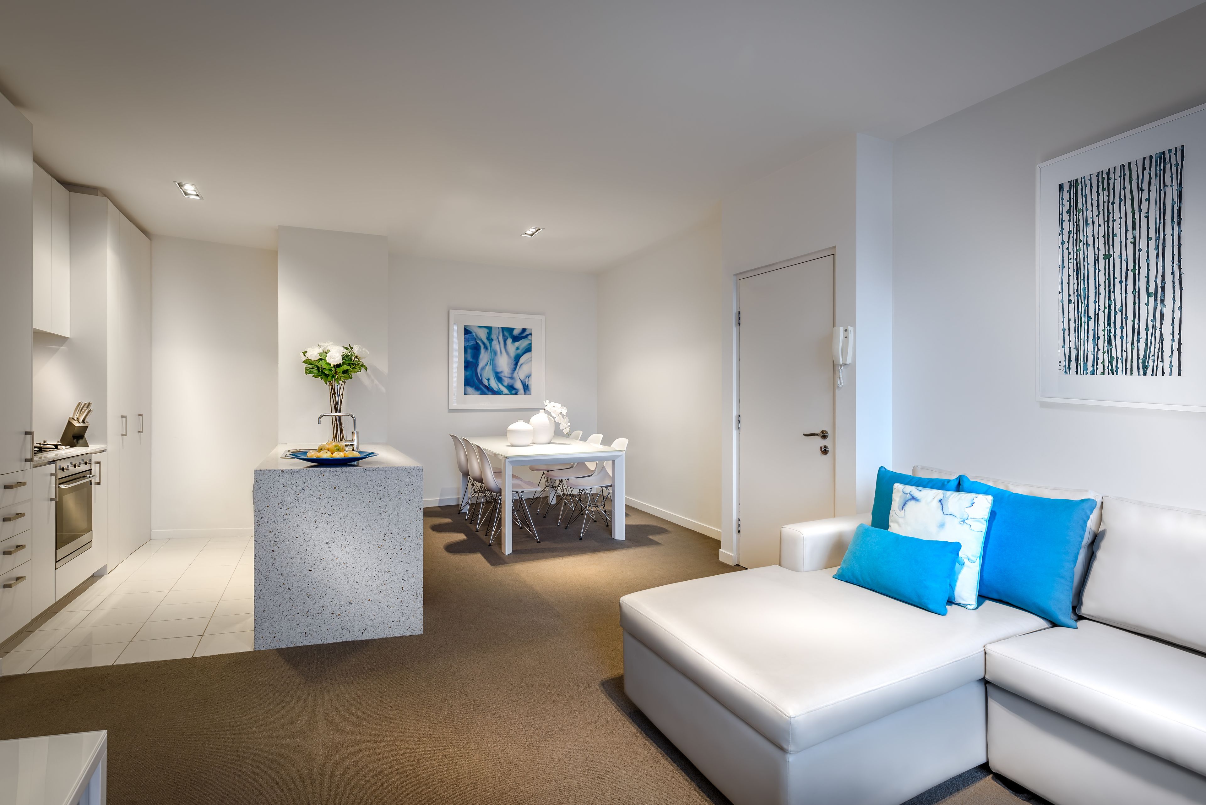 Un salon moderne avec un canapé blanc, un coin repas comprenant une table et des chaises, et une cuisine équipée d’armoires et d’un plan de travail.