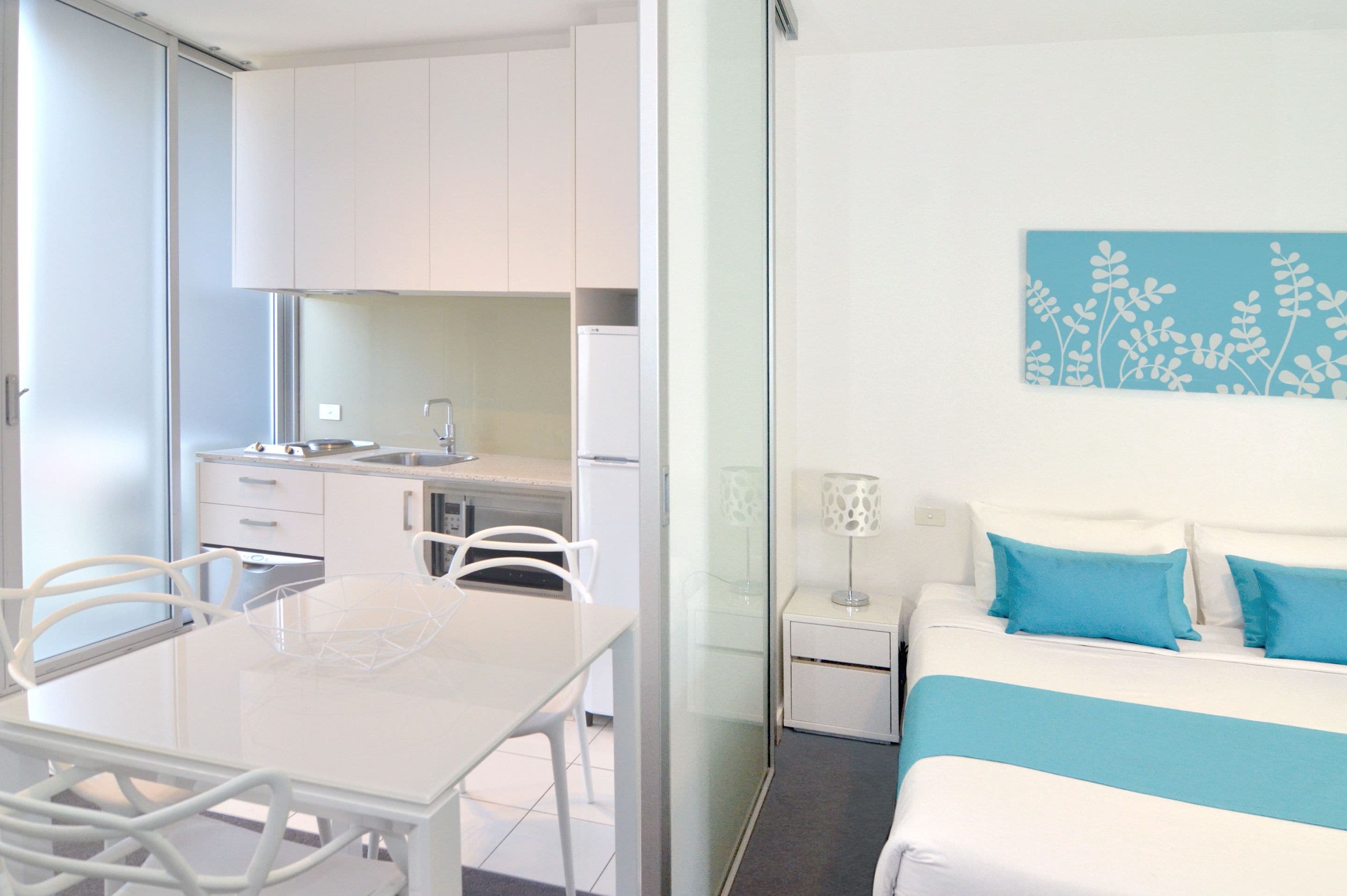 Una habitación de hotel moderna con una cama, mesita de noche y vistas al área de la cocina.