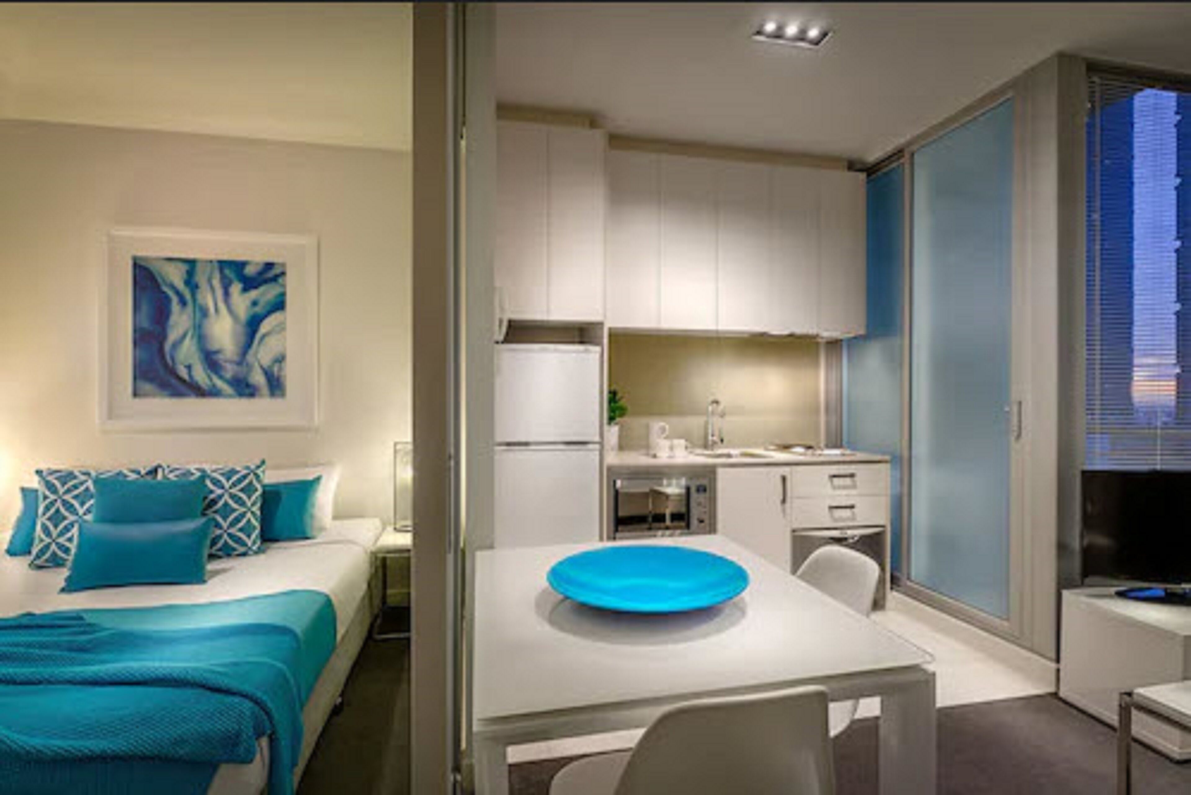 A modern bedroom with a bed, a bedside table, and a blue artwork on the wall.