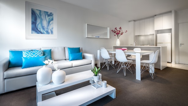 A modern living room with a sofa, coffee table, and dining area. - Milano Serviced Apartments (Melbourne)