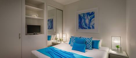 Una habitación de hotel moderna con una cama grande, un televisor, un espejo y una mesita de noche con una lámpara.
