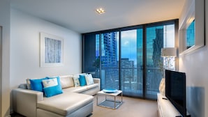 A modern living room with a sofa, a coffee table, a flat-screen TV, and large windows with a city view. - Milano Serviced Apartments (Melbourne)