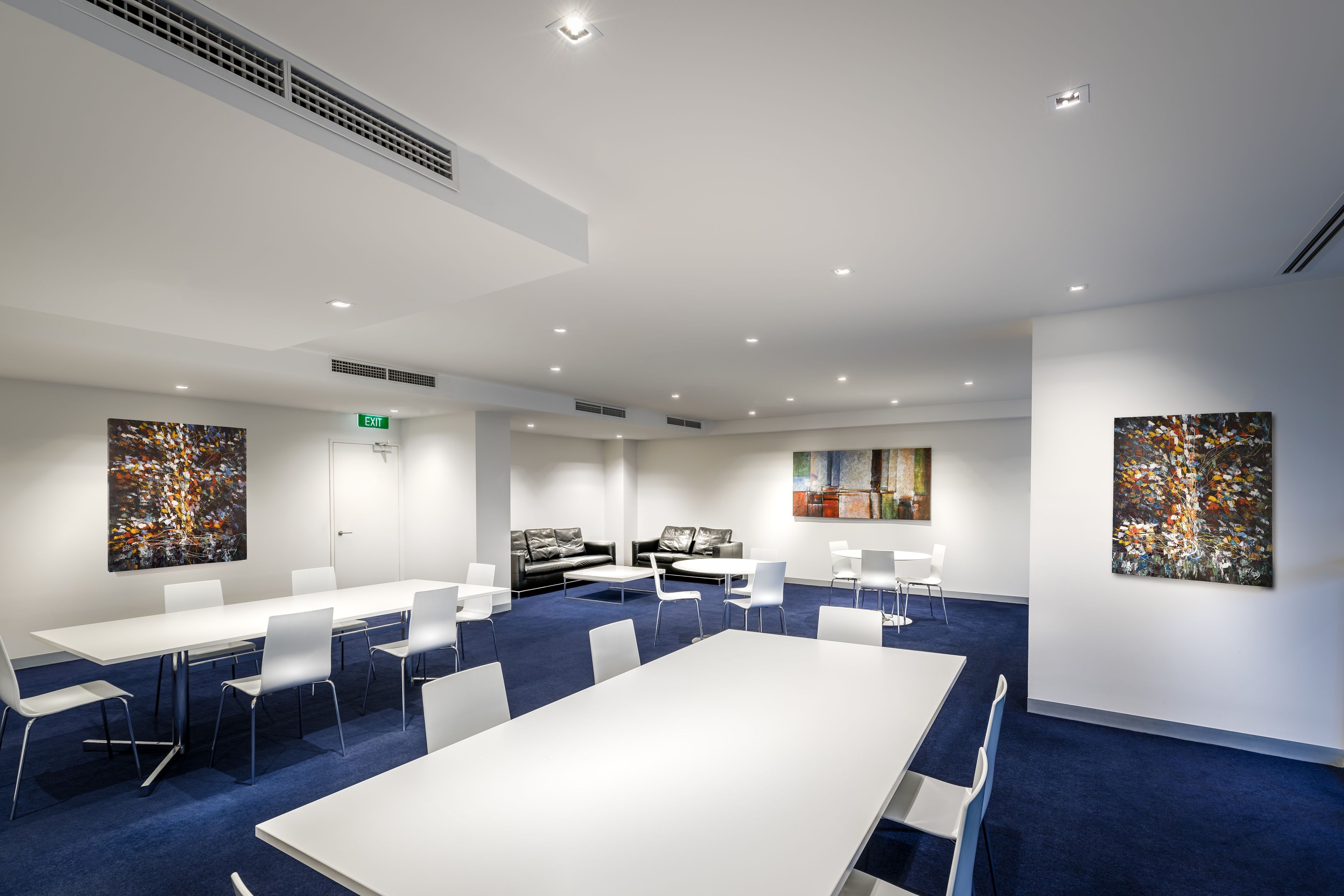 A modern conference room with white tables and chairs, a blue carpet, and abstract art on the walls.