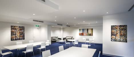 A modern conference room with white tables and chairs, a blue carpet, and abstract art on the walls.