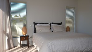 Une chambre à coucher avec un grand lit, deux tables de chevet et une fenêtre avec des stores.