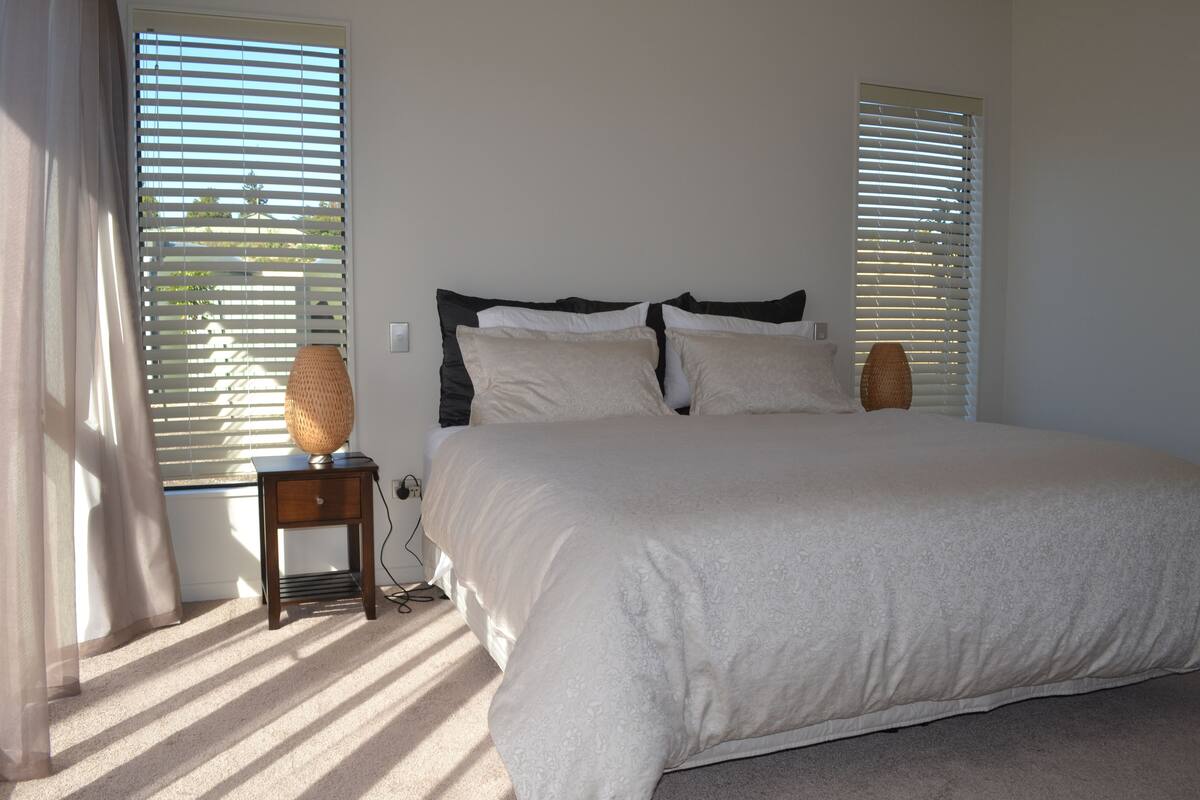 A bedroom with a large bed, two bedside tables, and a window with blinds.
