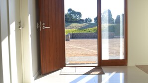 Une pièce dotée d’une porte en bois qui donne sur une porte vitrée, avec un sol carrelé et une vue sur un espace paysager à l’extérieur.