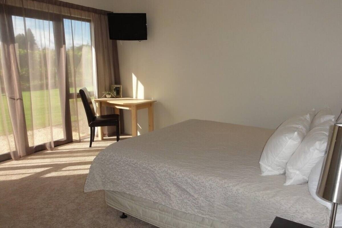 A hotel room with a large bed, a desk, a chair, and a TV mounted on the wall.