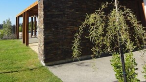 Une maison moderne avec une façade en pierre, une pergola en bois et un ciel d’un bleu éclatant.