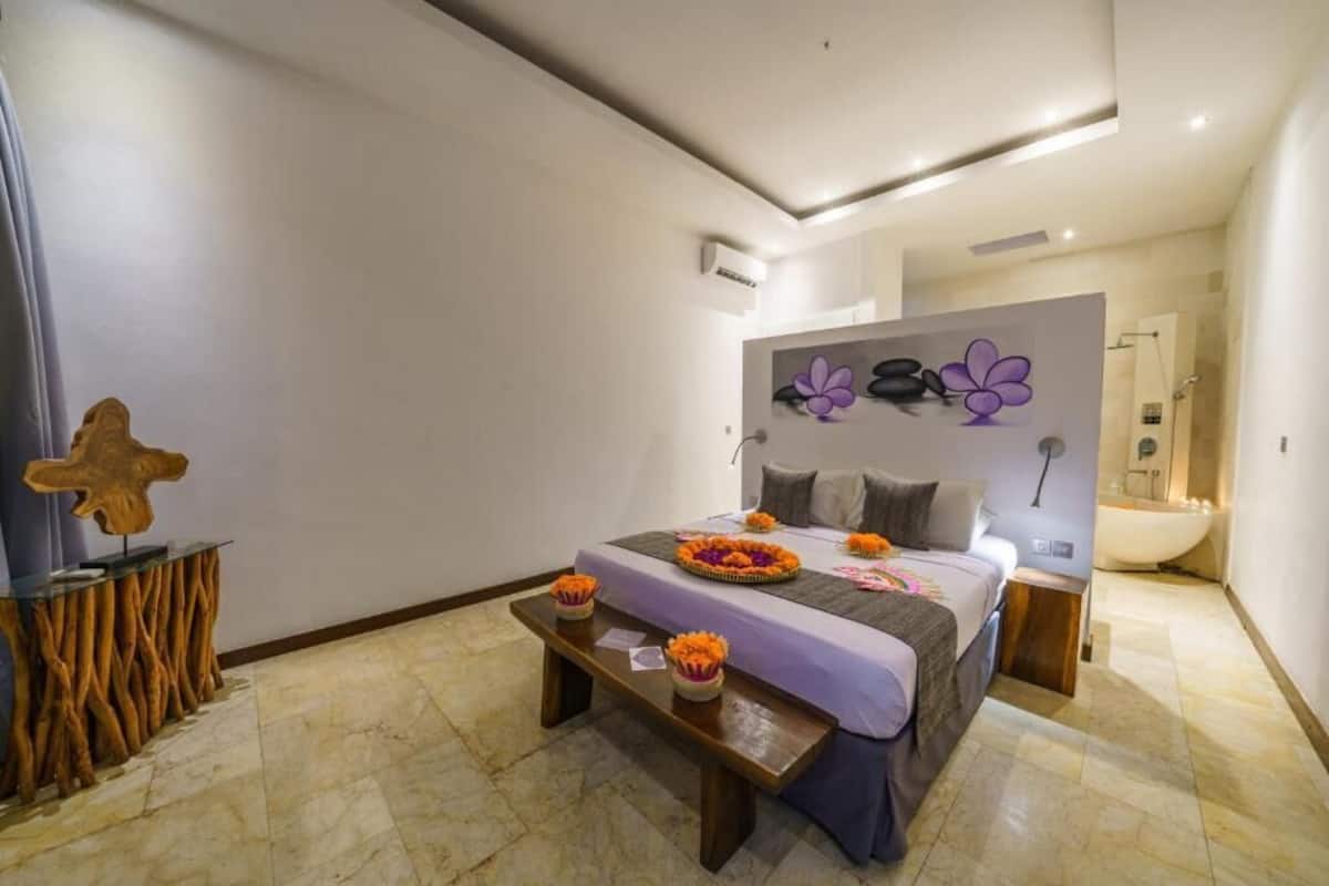 A modern bedroom with a large bed, a wooden side table, and a decorative wall piece.