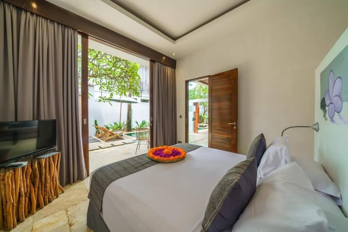 A hotel room with a large bed, a flat-screen TV on a wooden stand, and a view of a garden through a sliding door.