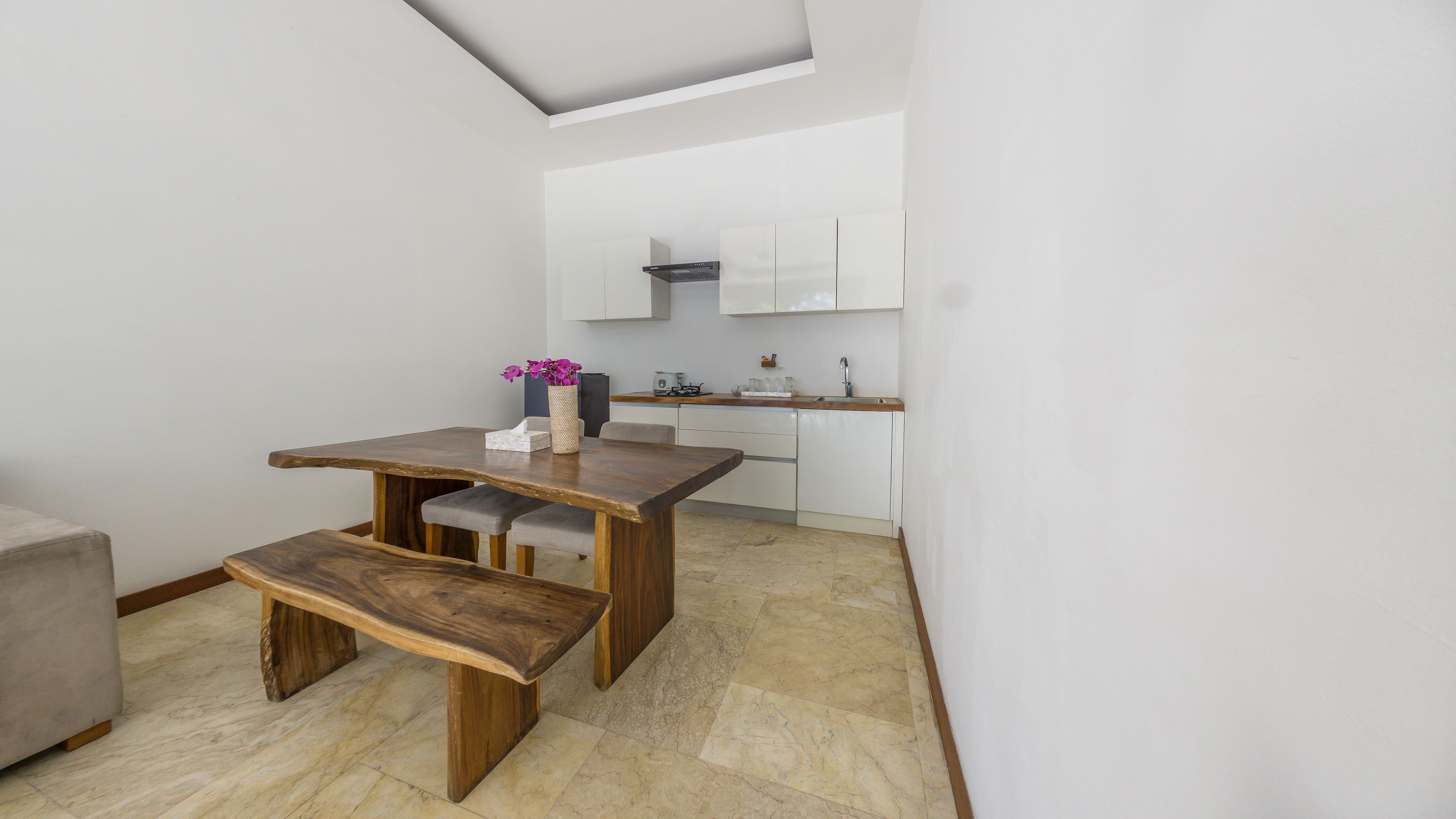 A compact kitchen with white cabinets, a wooden dining table, and a bench.