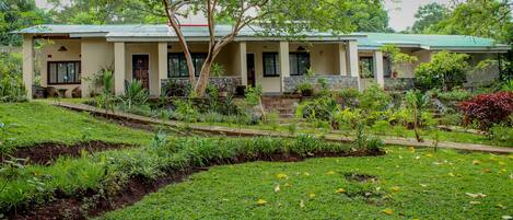 A two-story building with a green roof, surrounded by lush greenery and a well-maintained garden.