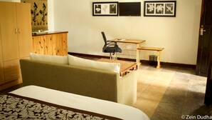 A hotel room with a bed, a sofa, a desk, and a chair. There are framed pictures on the wall and a television. - Villa 33 (Blantyre)