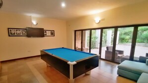 A pool table in a room with a large window, a flat-screen TV on the wall, and a blue sofa. - Villa 33 (Blantyre)