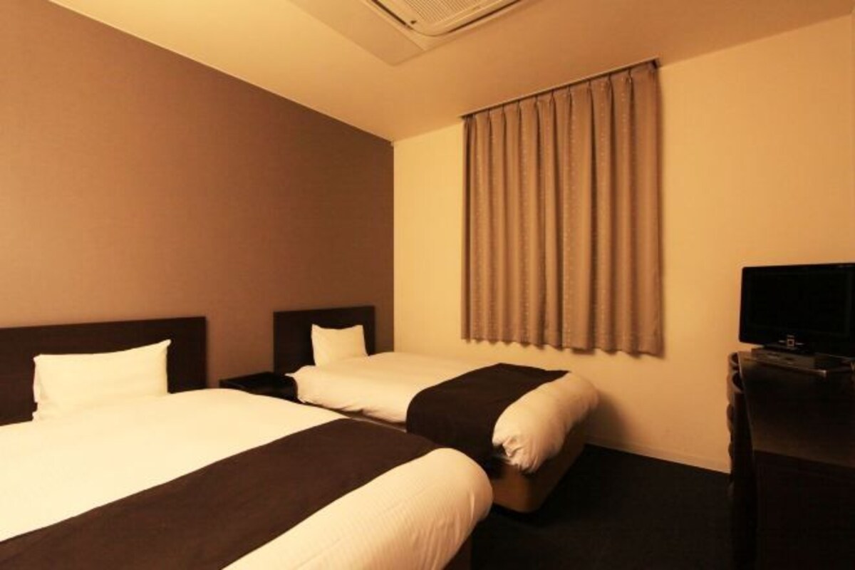 A hotel room with two beds, a television, and a window with curtains.