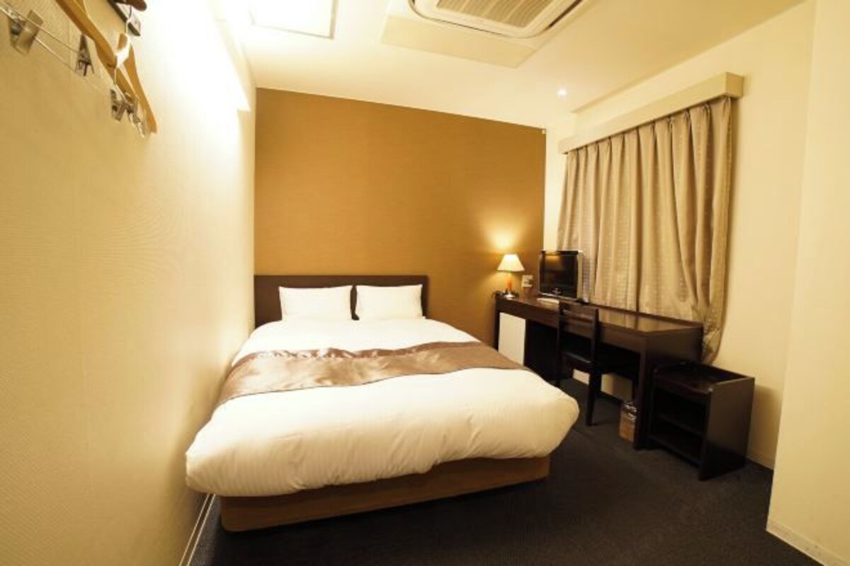 A hotel room with a bed, a desk, a chair, and a lamp.