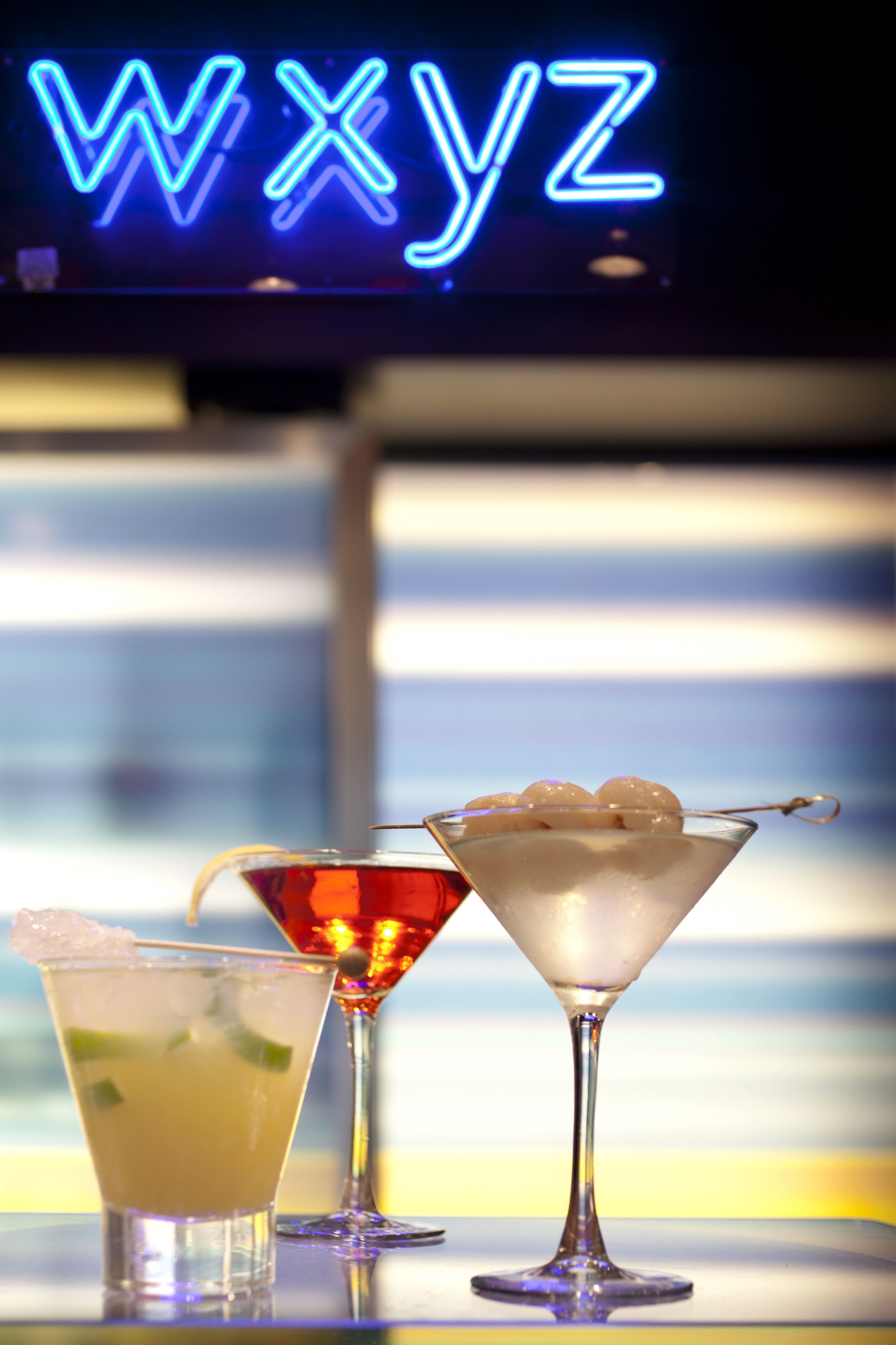 Tre cocktails på en bardisk med et neonskilt i baggrunden.