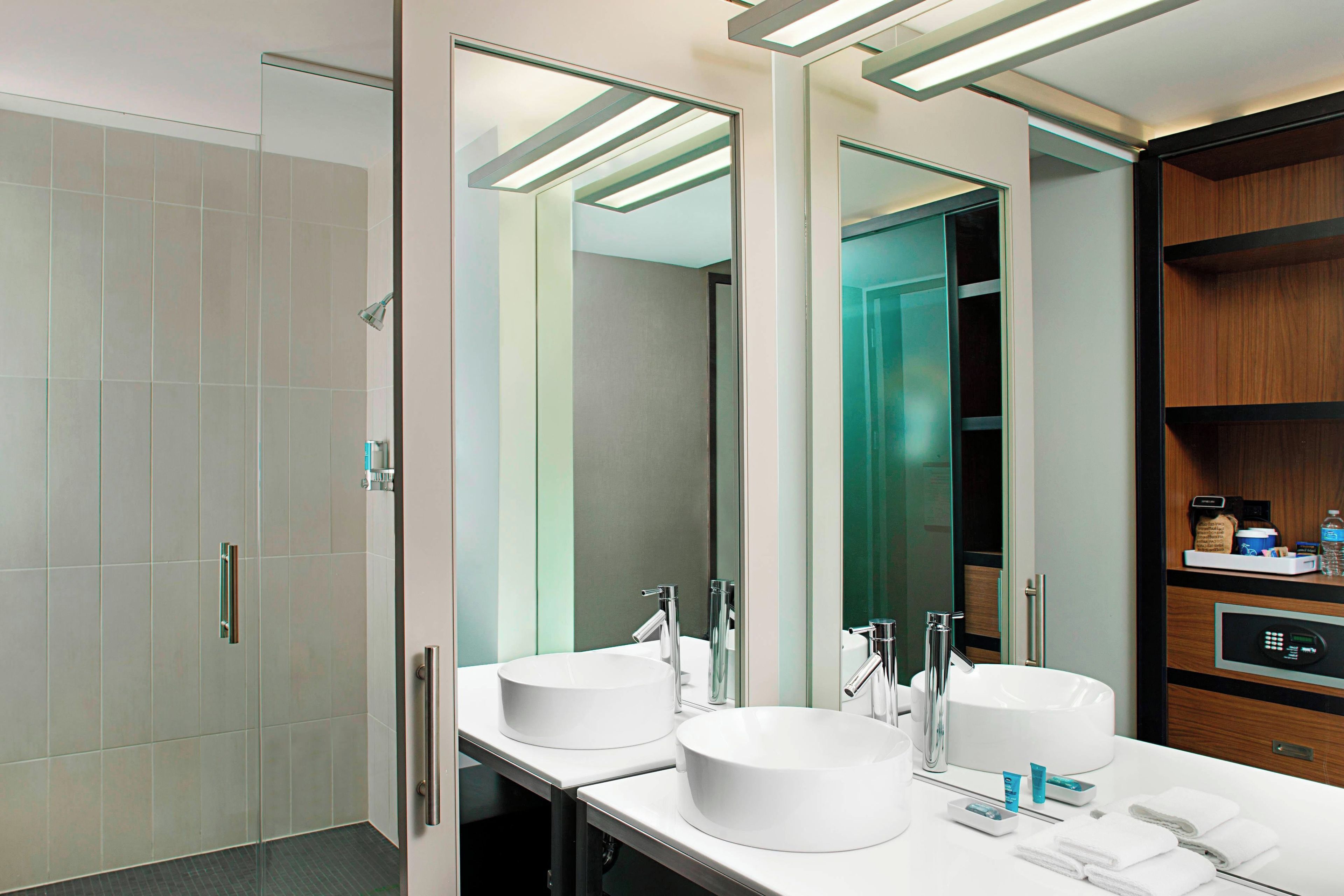 A modern bathroom with a large mirror, two sinks, and a shower.