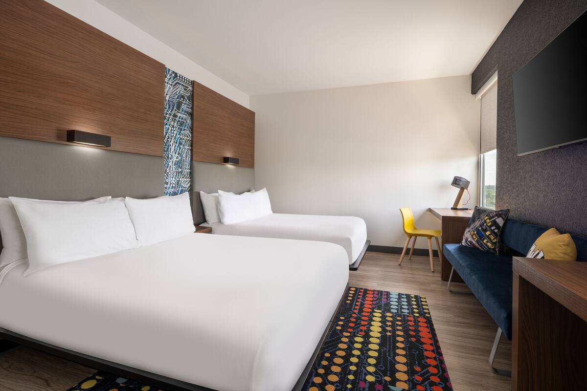 A hotel room with two beds, a desk, a chair, and a TV.