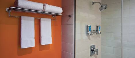 A bathroom with an orange wall, a glass shower enclosure, and two towels hanging on a metal rack.