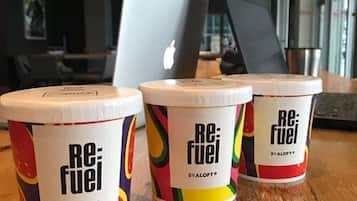 Three containers labeled 'Re:Fuel' by Aloft on a wooden table in a modern office setting.