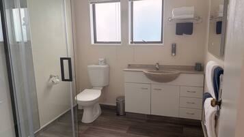 Baño con inodoro, lavabo y cabina de ducha de vidrio.