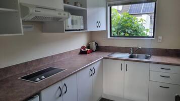 Una cocina con microondas integrado, hervidor de agua y lavabo. Se ve un ventanal con vistas a zonas verdes.