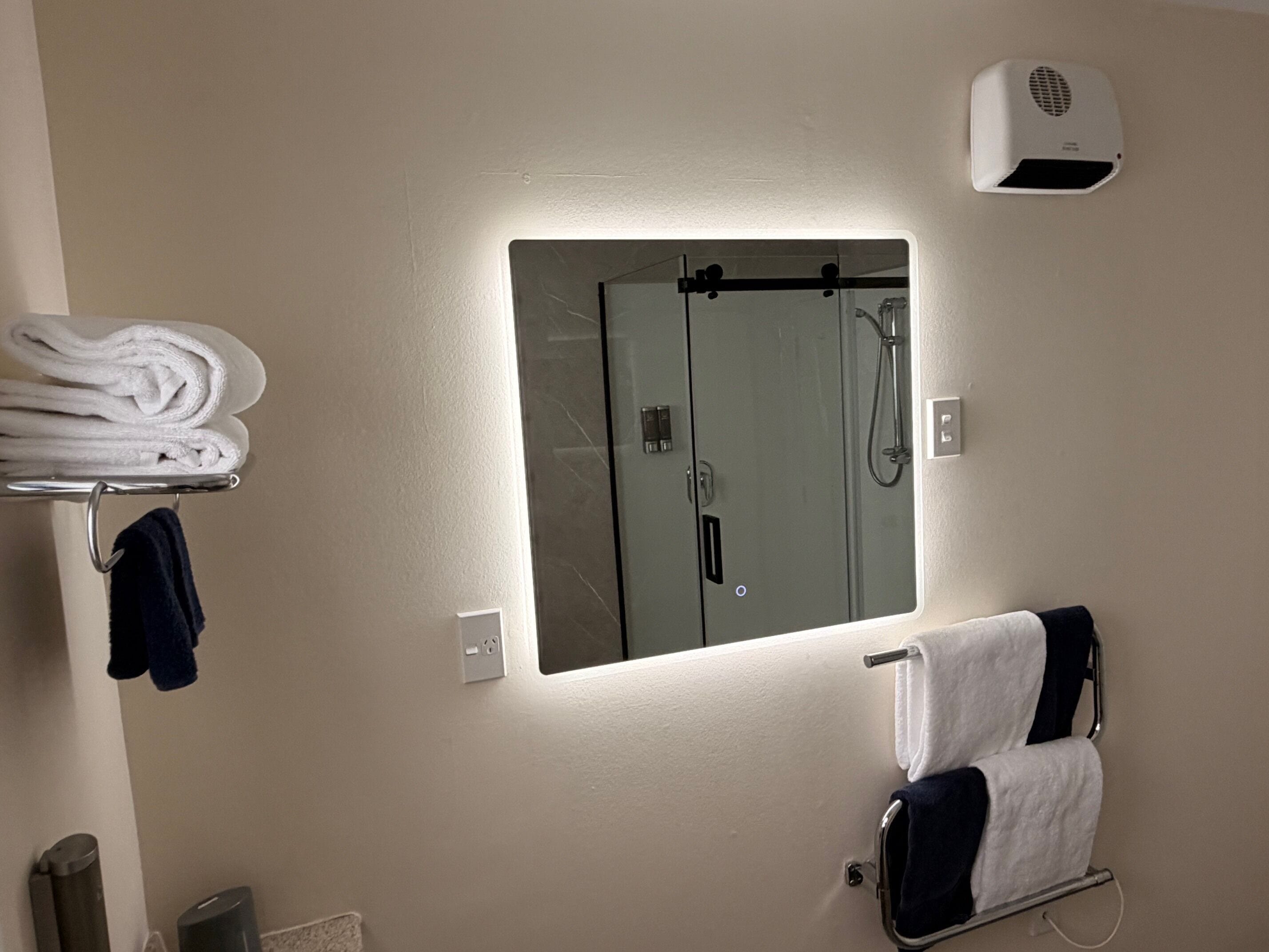 Une salle de bain équipée d’un miroir, d’un porte-serviettes et d’un sèche-mains.