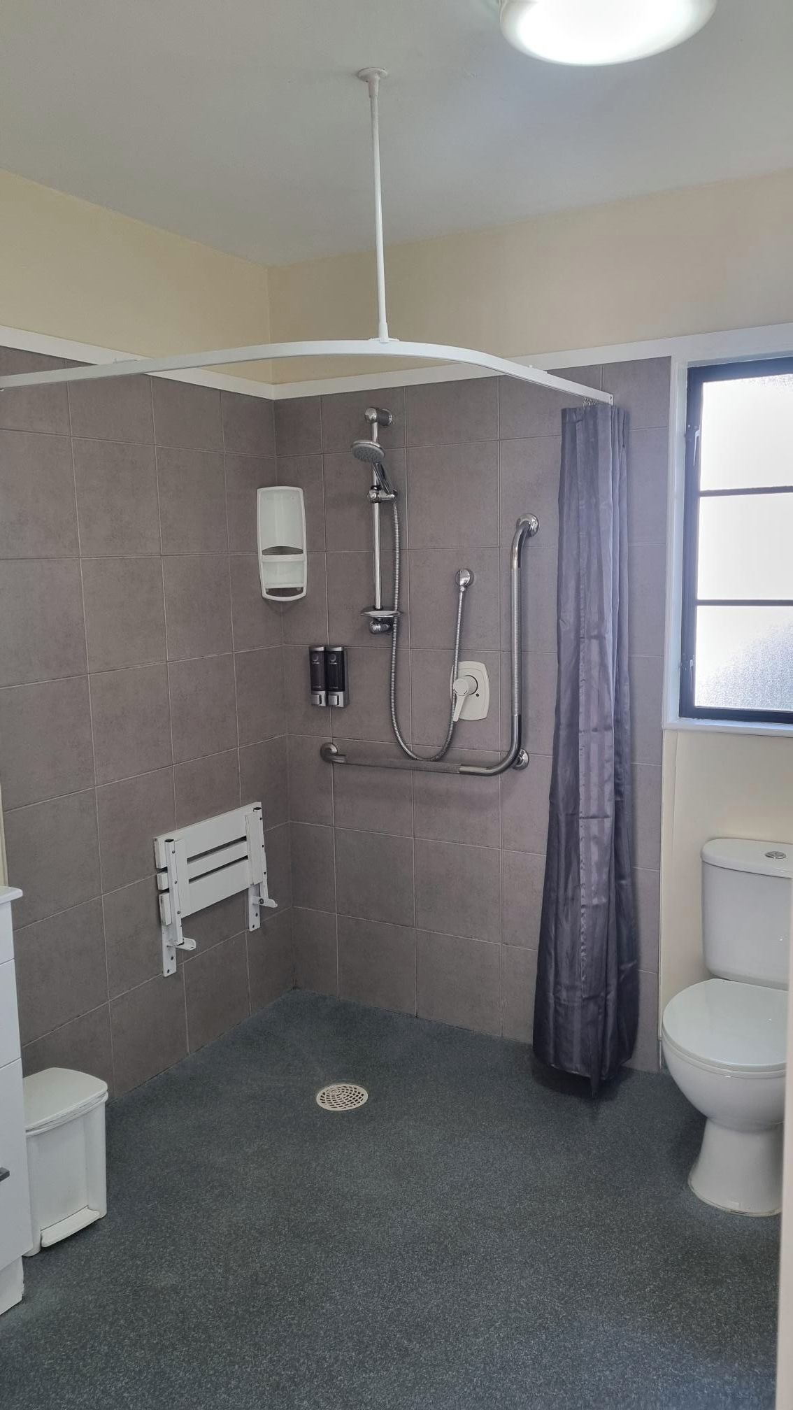 Une salle de bain avec une douche, des toilettes et une fenêtre.