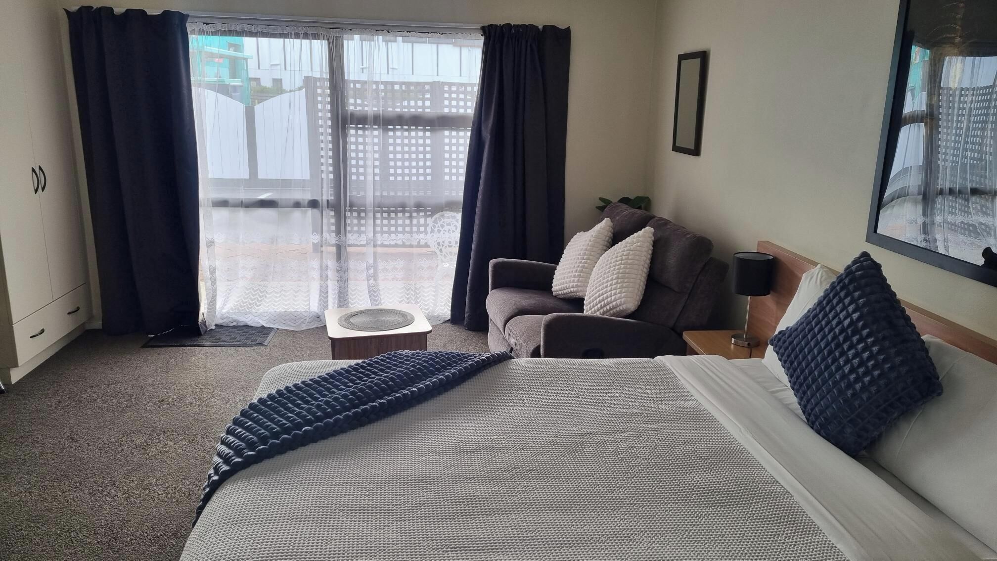 Habitación de hotel con cama, una silla, una mesita y vistas a un edificio a través del ventanal.
