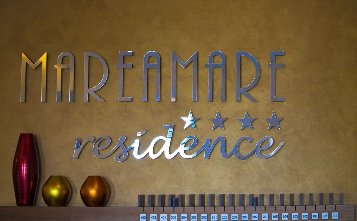 A wall with the words "MAREAMARE residence" and three decorative vases.