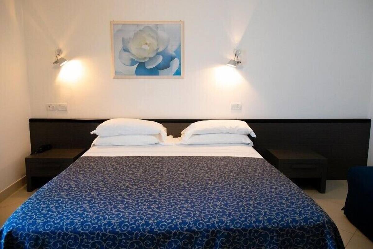 Una habitación de hotel con una cama grande, dos mesitas de noche, un cuadro colgado en la pared y dos lámparas de pared.