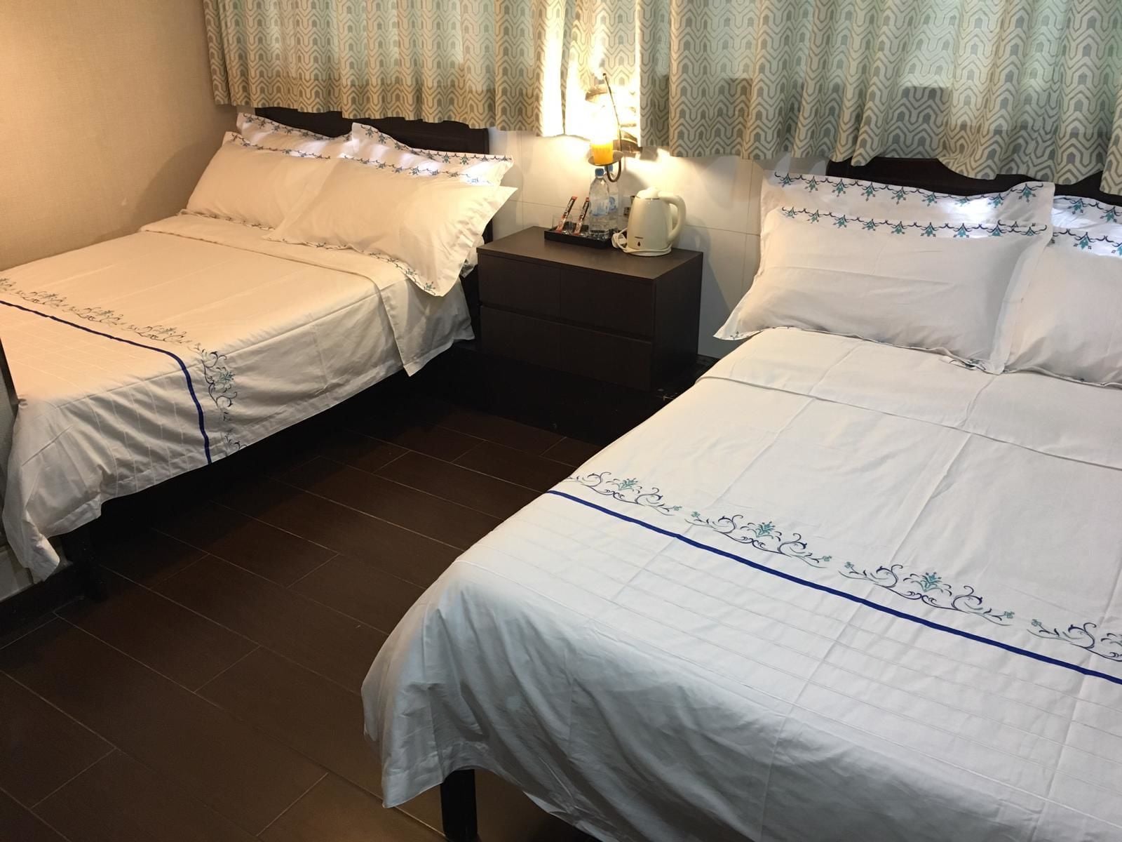 A hotel room with two beds, a nightstand with a lamp, and a window with curtains.