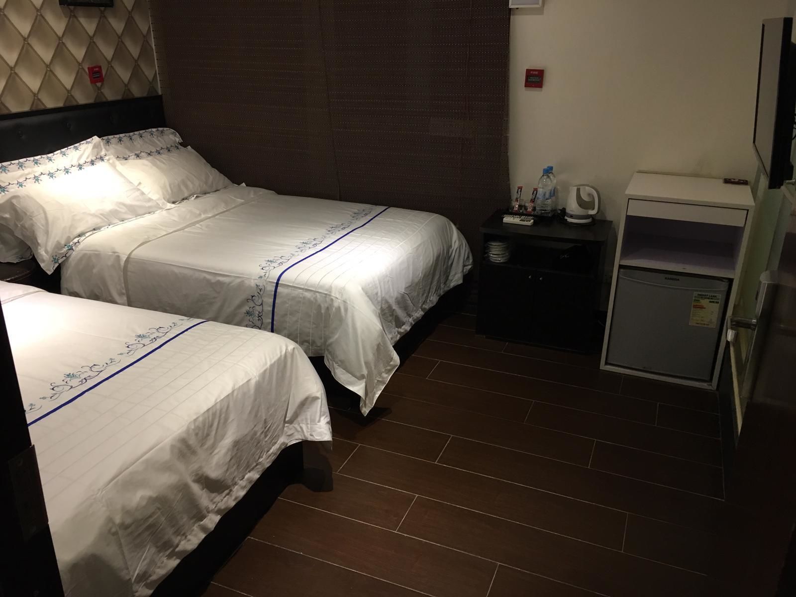 A hotel room with two beds, a small table with a water bottle, a microwave, and a refrigerator.
