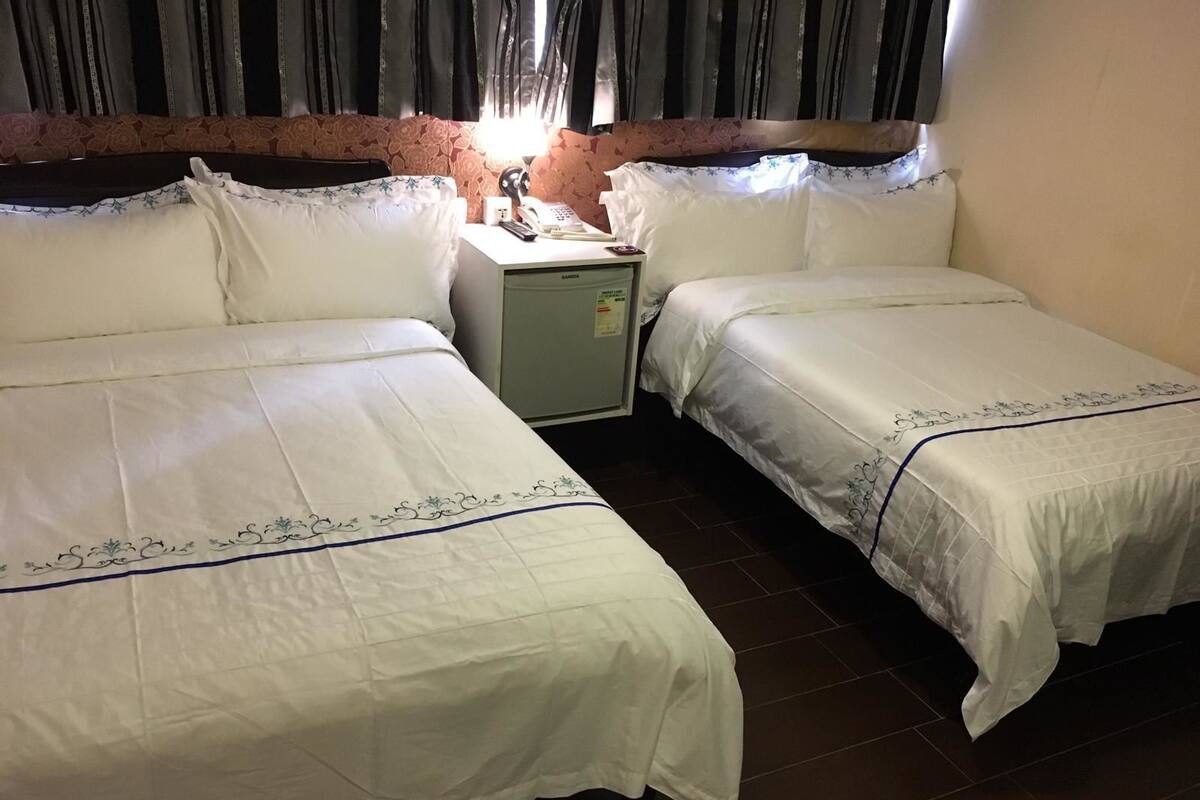 A hotel room with two single beds, a small desk with a lamp, and a window with curtains.