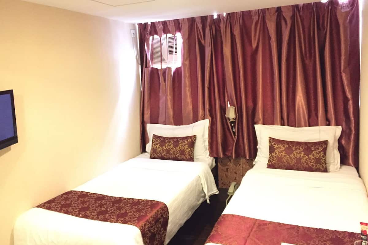 A hotel room with two beds, a television on the wall, and a window with curtains.
