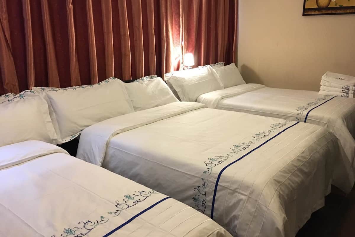 A hotel room with two beds, each with white bedding and blue trim. There is a painting on the wall above the beds.