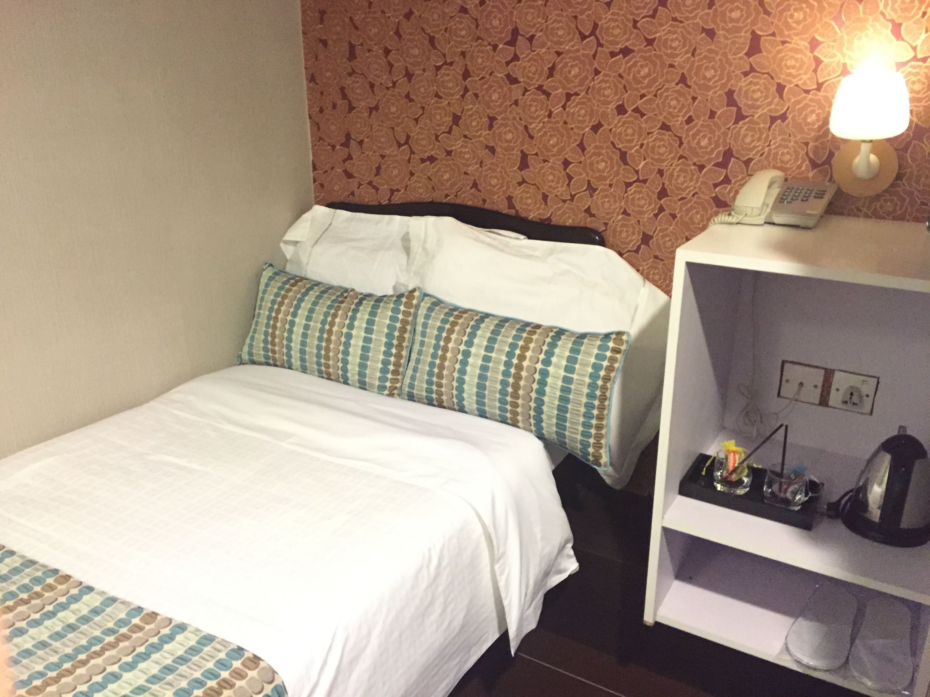A hotel room with a bed, pillows, a nightstand, a lamp, and a phone.