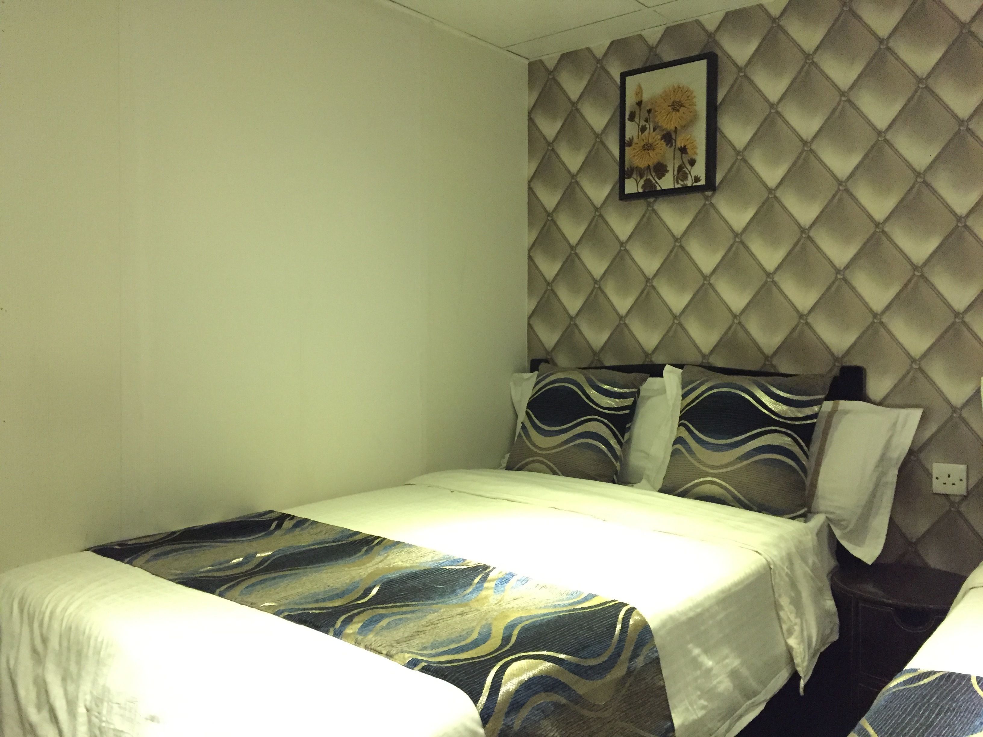 A hotel room with a bed, a headboard, and a wall-mounted picture.