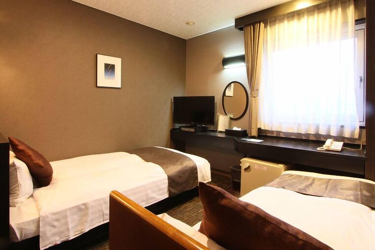 A hotel room with two beds, a TV, a desk, a mirror, and a window with curtains.