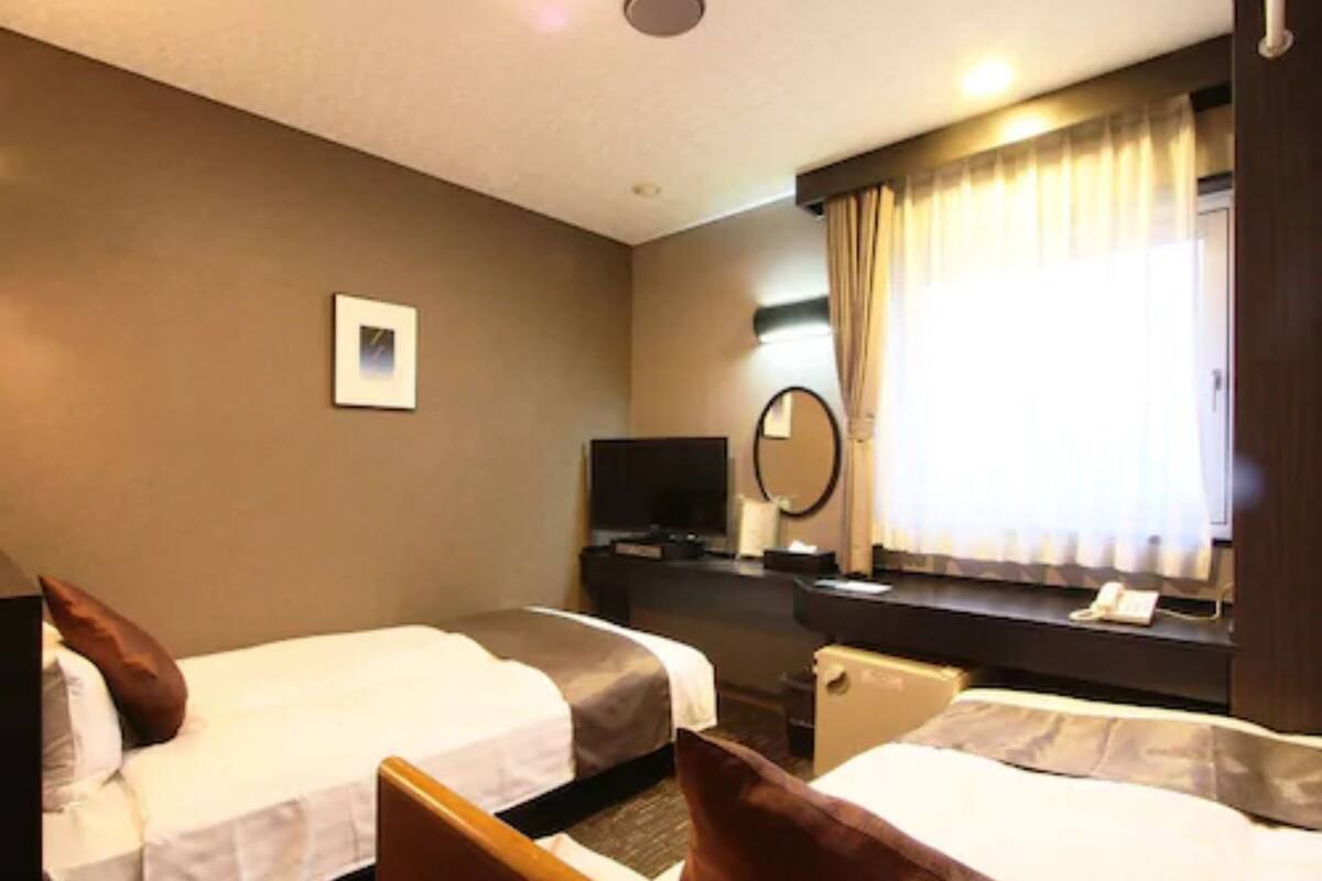 A hotel room with two beds, a TV, a desk, a mirror, and a window with curtains.
