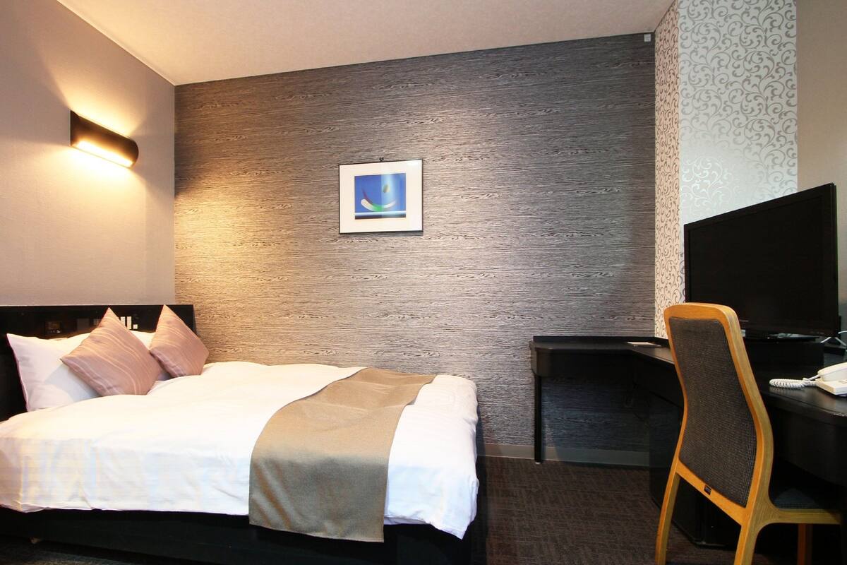 A hotel room with a bed, a desk, a chair, a TV, and a picture on the wall.