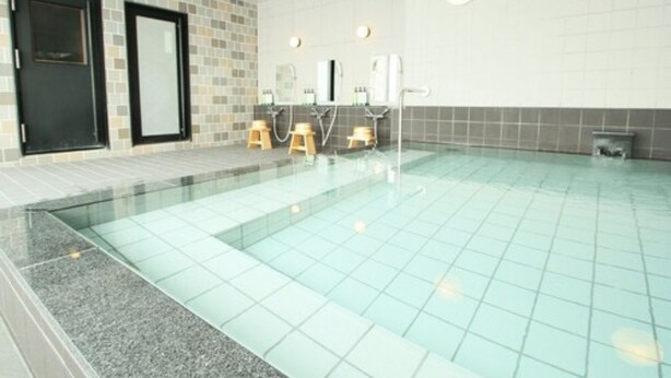 Una piscina con paredes y suelo de azulejos, dos taburetes de madera y una puerta negra.