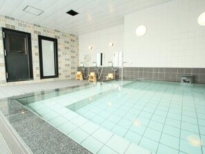 A swimming pool with tiled walls and a tiled floor, two wooden stools, and a black door. - Hotel AreaOne Chitose (Chitose)
