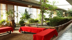 Un comedor interior con mesas cubiertas de manteles rojos, rodeado de plantas en macetas y una valla de bambú.
