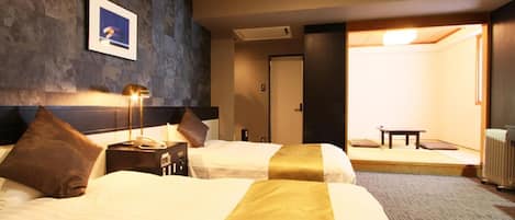 A hotel room with two beds, a bedside table with a lamp, a picture on the wall, and a view of a traditional Japanese room.