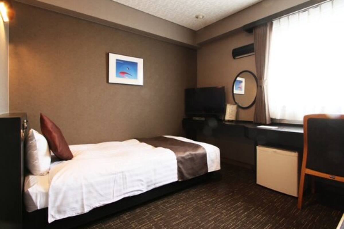 A hotel room with a bed, a desk, a chair, a TV, a mirror, and a window with curtains.